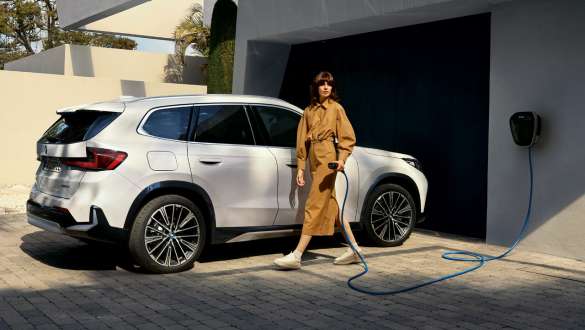 BMW iX1 U11 BEV 2022 Entrée du garage BMW iX1 U11 BEV 2022 Mineralweiß metallic ¾ vue de profil entrée du garage en stationnement