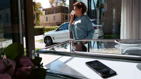 Remote Software Upgrade, BMW X5 Femme en train de boire une tasse de café tandis qu’elle met à jour le logiciel de sa BMW X5 par la fonction Remote Software Upgrade G05 2018