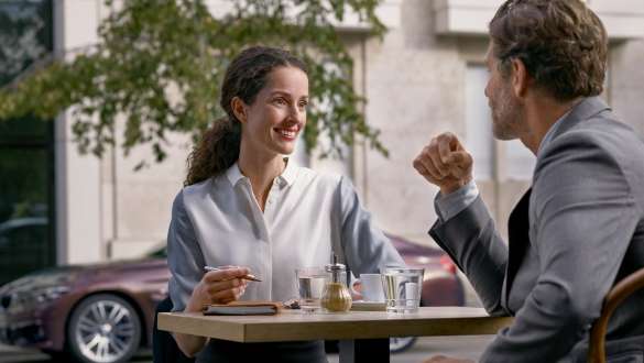 Service Données de flotte BMW Service Après-vente entreprises BMW : Un homme et une femme sont dans un café. On voit une BMW à l’arrière-plan