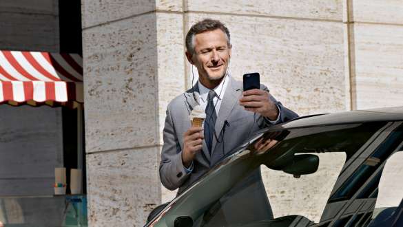 Services de Réparation et d’entretien d’origine BMW Services de Réparation et d’entretien d’origine BMW : Un homme avec un smartphone dans la main se tient près d’une BMW