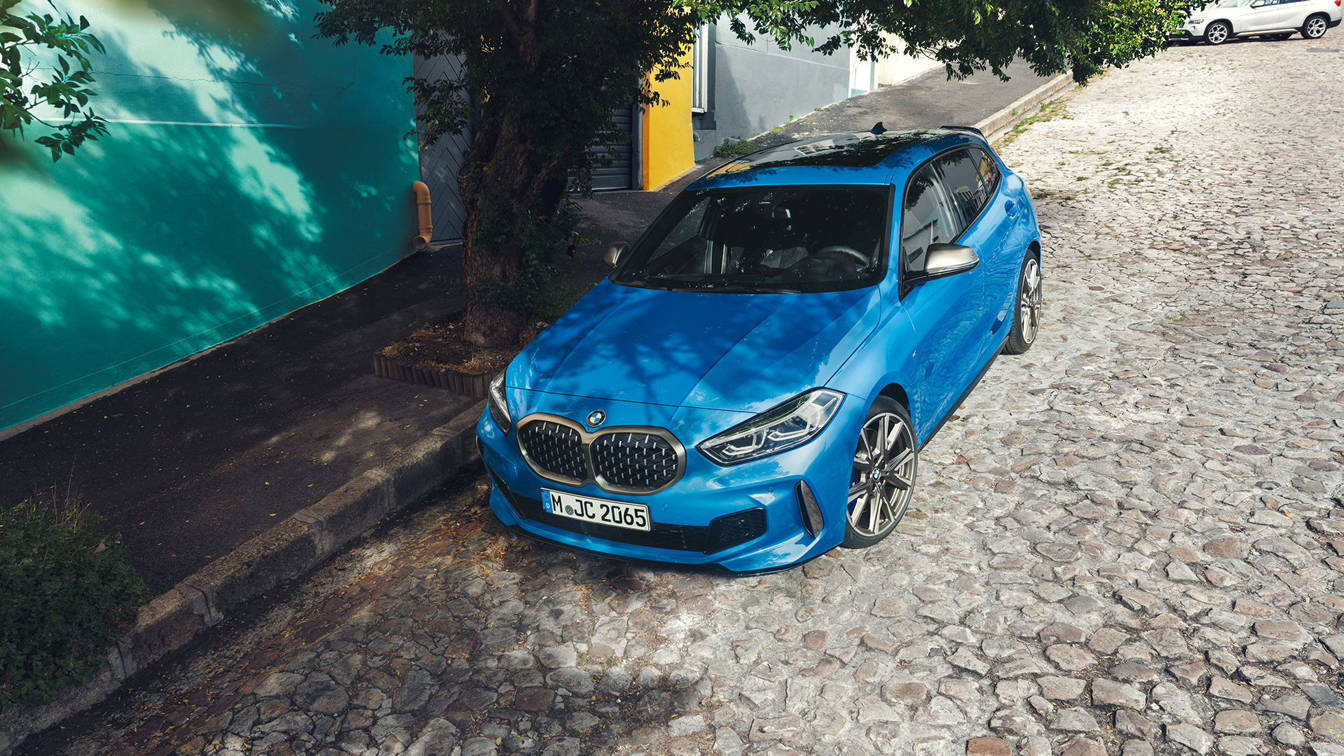1 Series BMW at the roadside. 1 Series BMW in Misano Blue metallic, three-quarter front view, parking at the roadside from a bird’s eye view.
