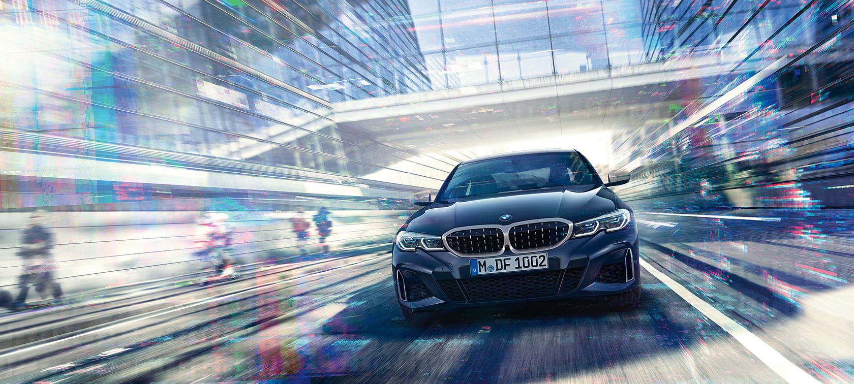 BMW Série 3 Berline, vue avant de la BMW M340i xDrive. Vue avant de la BMW M340i xDrive Berline qui roule entre des bâtiments de verre dans la ville.