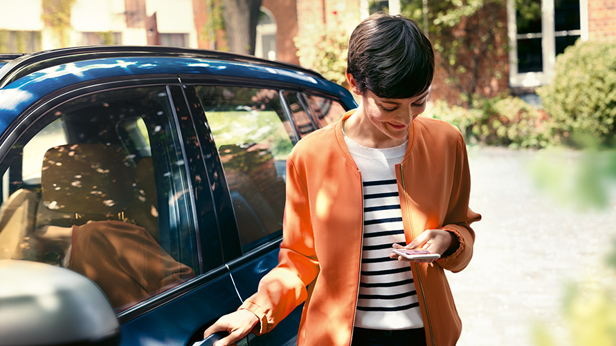BMW Service femme avec smartphone devant la porte de sa BMW BMW Service femme avec smartphone devant la porte de sa BMW