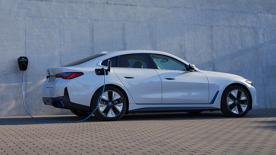 Vue de profil avec une borne de recharge BMW Wallbox BMW i4 eDrive40 G26 2021 BMW i4 eDrive40 G26 2021 Mineralweiß, vue de profil devant un mur avec une borne de recharge BMW Wallbox