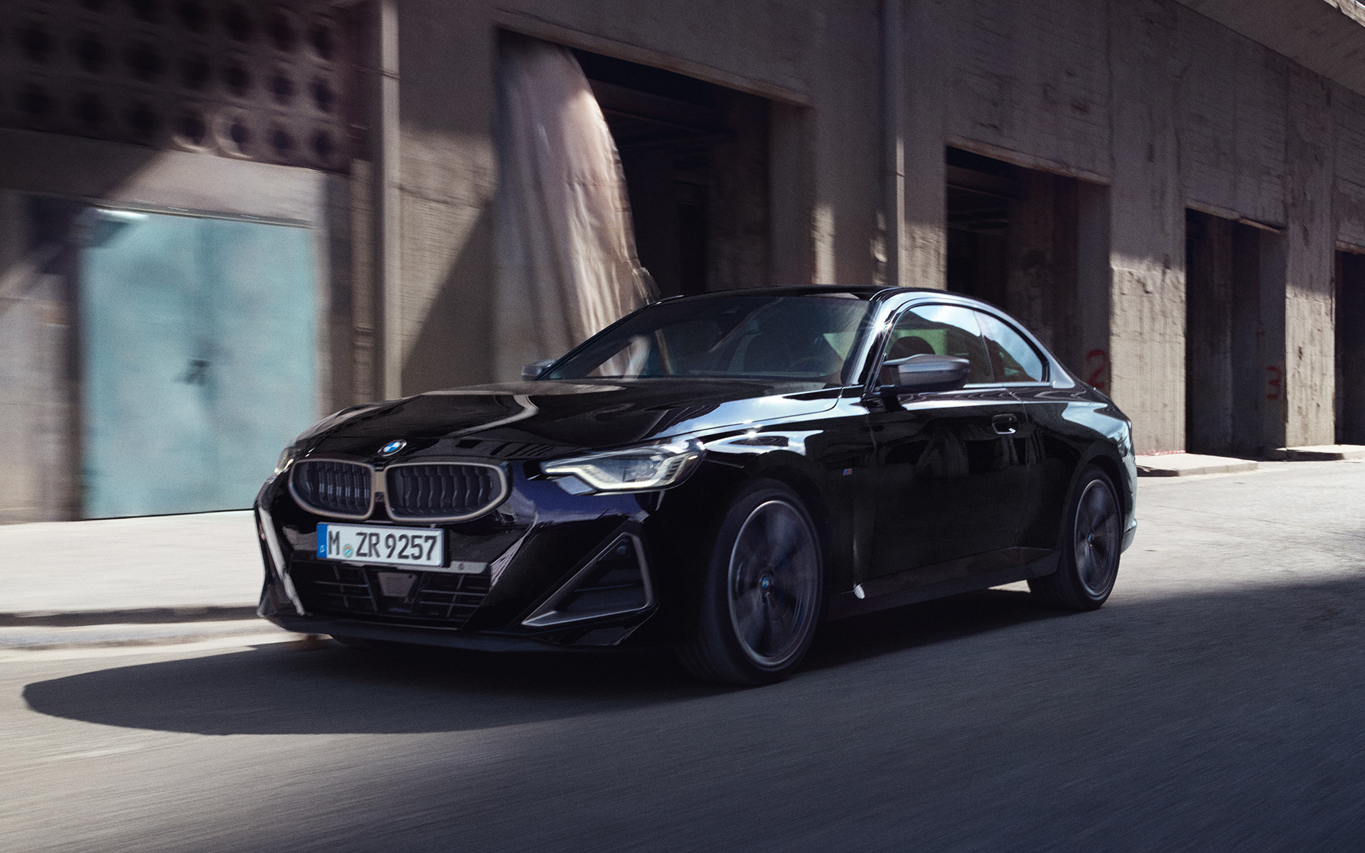 BMW M240i xDrive Coup&eacute; G42 2021 Black Sapphire metallic, vue de trois quarts de profil en mouvement devant des entrep&ocirc;ts
