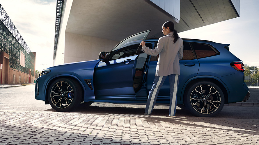 BMW X3 M Competition F97 LCI 2021 Vue de profil avec portière ouverte et mannequin femme BMW X3 M Competition F97 LCI restylage 2021 Frozen Marina Bay Blau metallic Vue de profil avec portière ouverte et mannequin femme