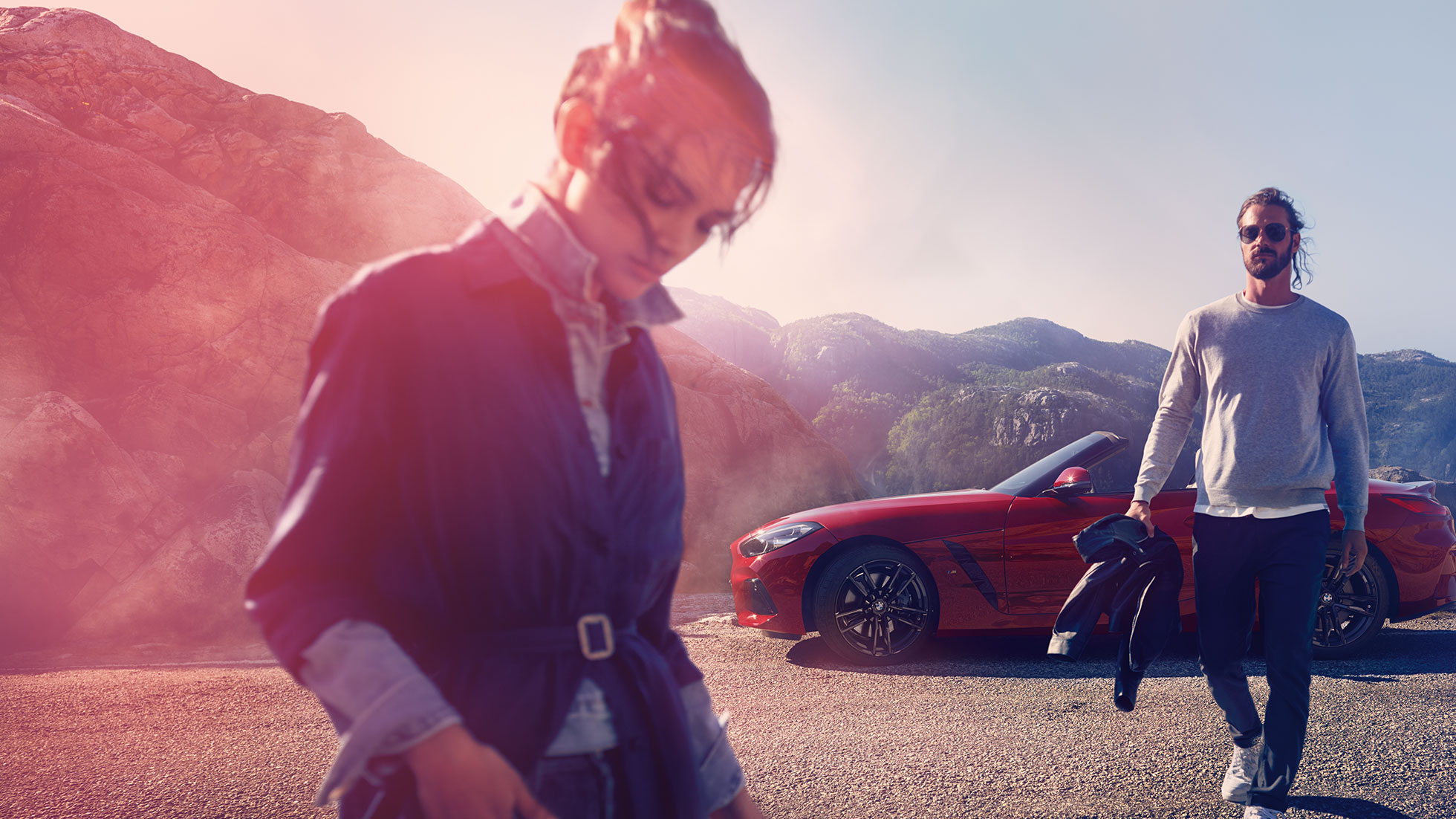La BMW Z4 Roadster devant un paysage de montagnes Homme et femme devant la BMW Z4 Roadster avec à l’arrière-plan un paysage de montagnes