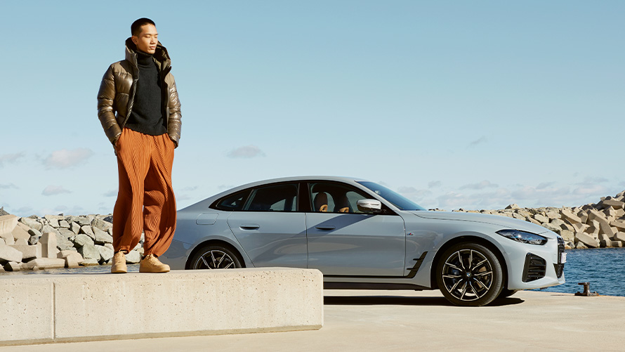 BMW Service Inclusive BMW G26 Homme debout sur un rebord de pierre avec un véhicule BMW en arrière-plan